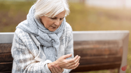 Woman sitting on a brown bench in the fall, massaging her wrist due to arthritis.